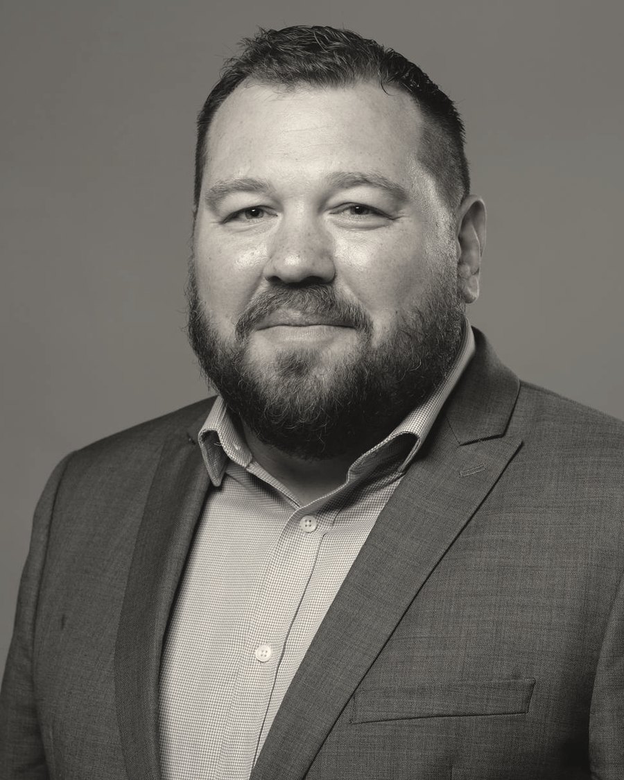 Black and white portrait of Teddy Lyngaas in a grey suit jacket.