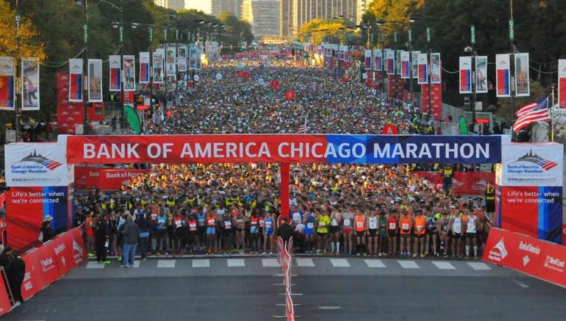 A packed marathon finish line seen from above, runners filling the street between grandstands.