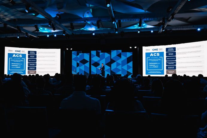 A general session stage with a bold blue and yellow angular scenic wall and side screens.