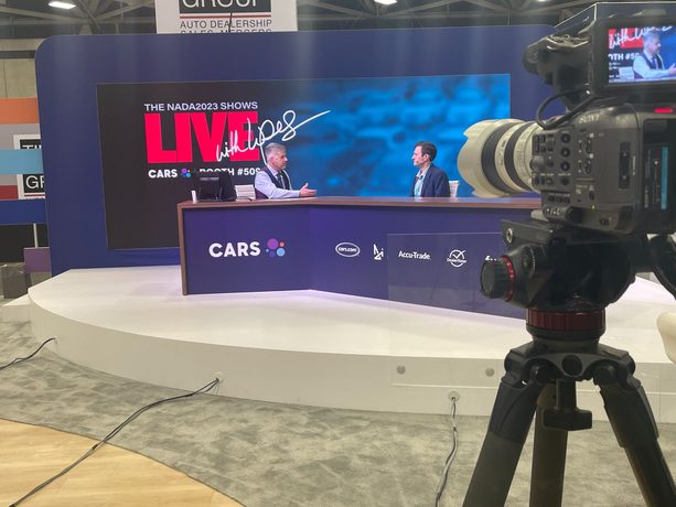 A broadcast camera and monitor stack set up at the back of a bright meeting room.