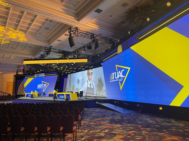 A teal-lit panel set with lounge chairs, a lectern and a large content screen.