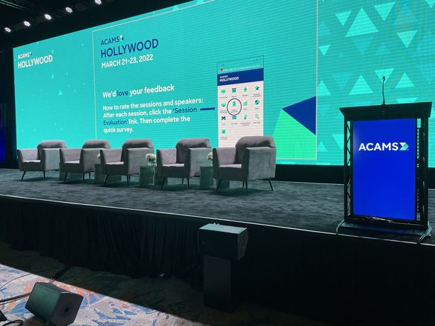 A wide blue general session stage with a speaker and large presentation screens.