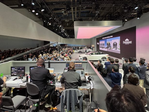 A trade show floor crowded with attendees between tall exhibit structures.