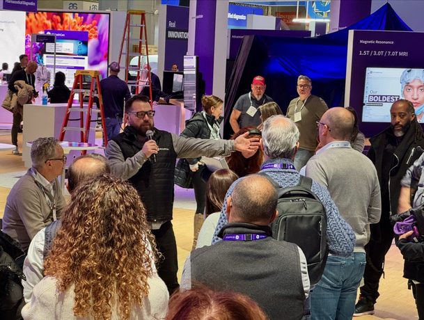 A busy attendee reception area with screens and exhibit signage overhead.