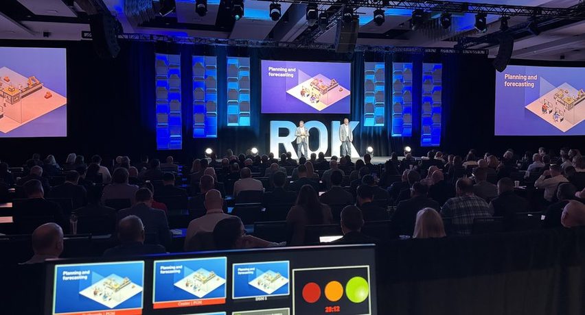 A corporate general session with a blue scenic stage, side screens and a full audience.